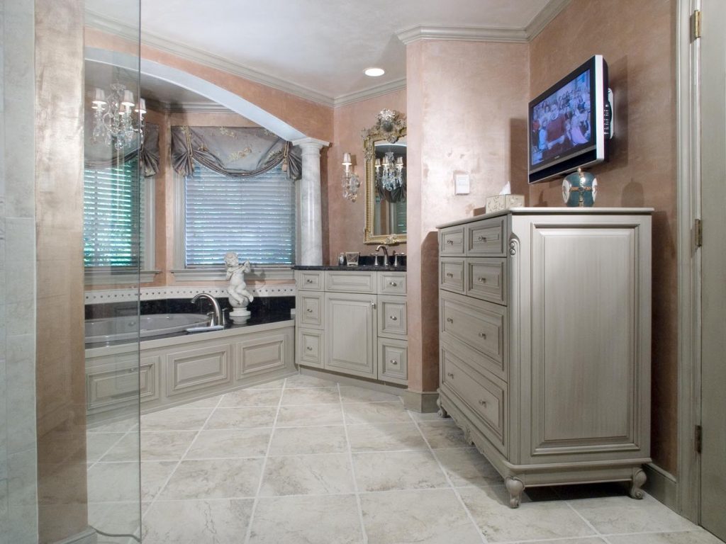luxurious bathroom with cabinetry, TV, pillar and drop-in tub in oasis