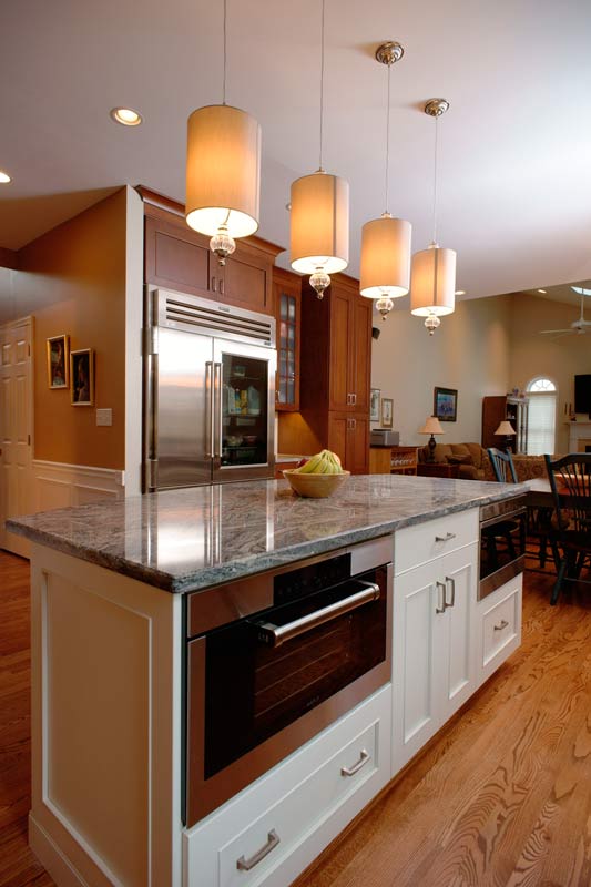 Central kitchen island topped with Scottish meadow granite with overhead hanging pendant lights by Morris Black